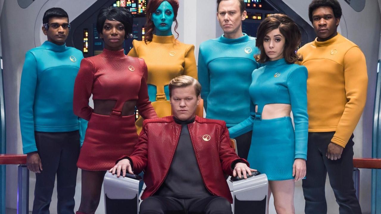 Photo de groupe de l’équipage de « USS Callister » (Black Mirror), en uniformes colorés de style science-fiction rétro, sur le pont d’un vaisseau